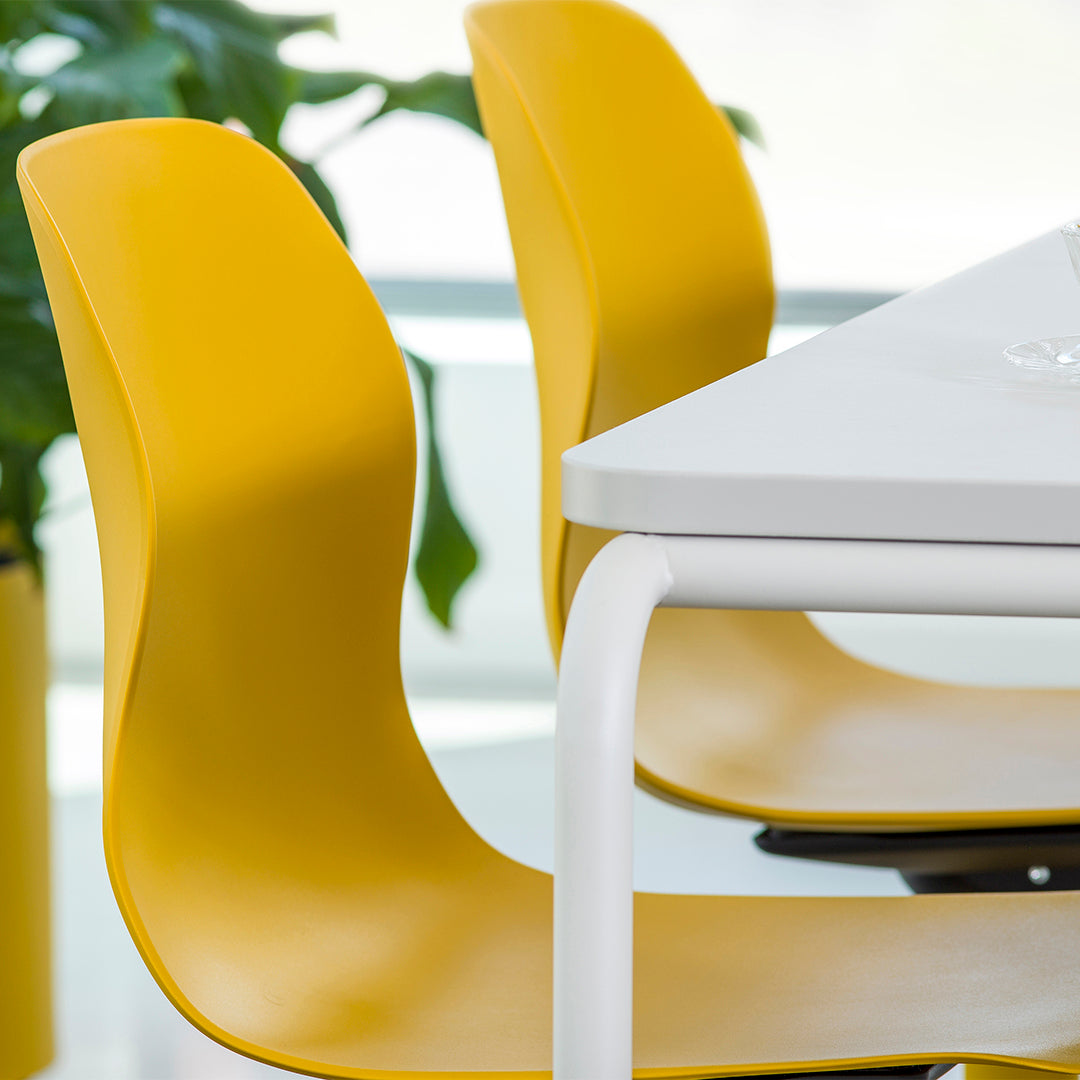 Yellow modern chairs with smooth curves beside a white table and green plant accents. Bright color palette for contemporary style.