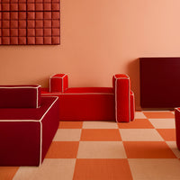 Red and burgundy sofas with cream piping against a peach wall and orange checkered flooring. Modern, vibrant design.