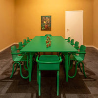 Modern green table and chairs against a warm yellow wall, featuring small potted plants as decor.