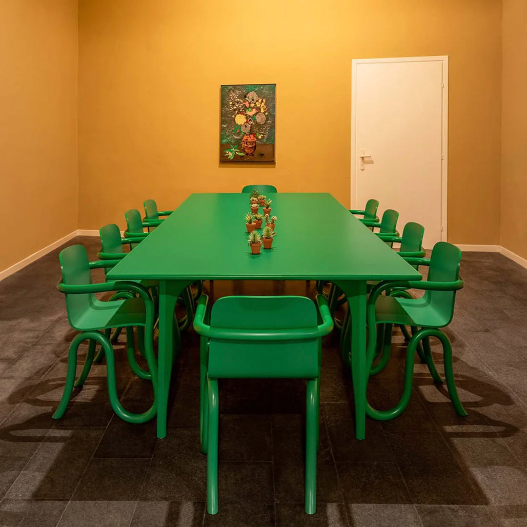 Green dining table with matching chairs against a warm orange wall and dark gray flooring, creating a vibrant contrast.