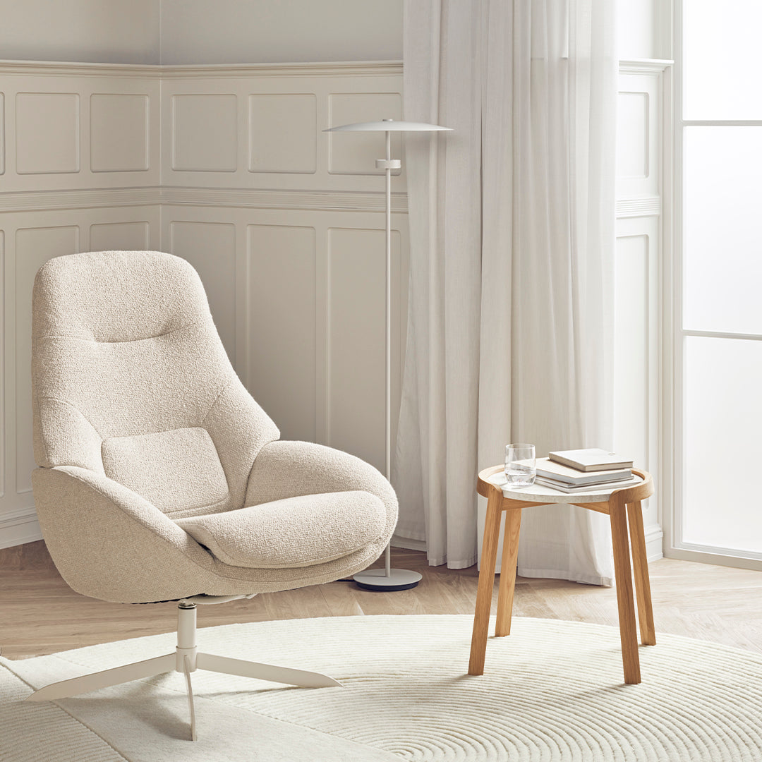 Light beige armchair with smooth upholstery, paired with a wooden table and soft beige rug for a cozy, neutral aesthetic.