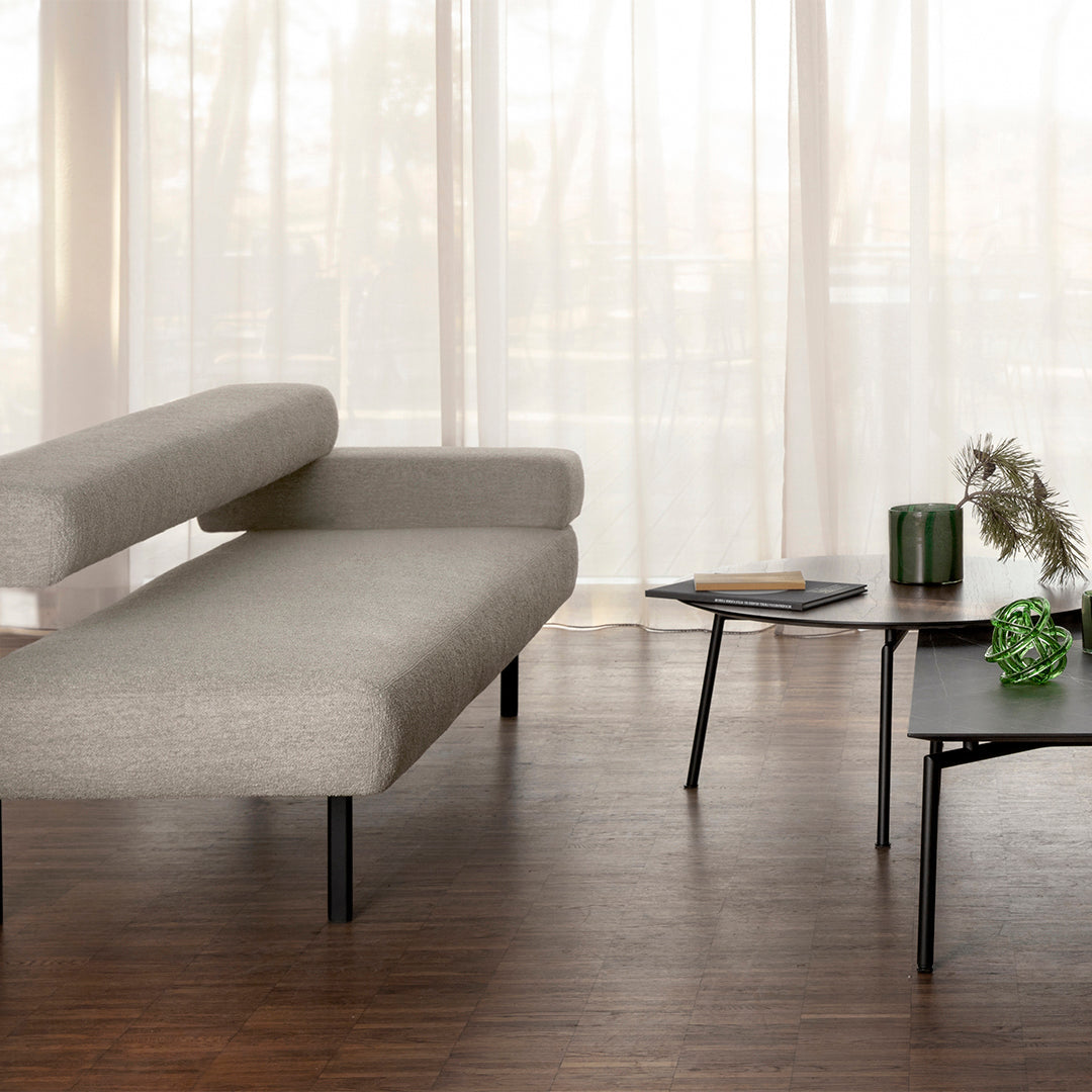 Gray textured sofa with minimalist black legs, green decorative items, and natural wood flooring in a bright, airy space.