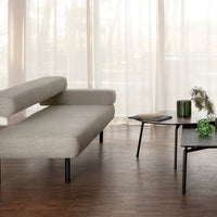 Gray textured sofa with minimalist black legs, green decorative items, and natural wood flooring in a bright, airy space.