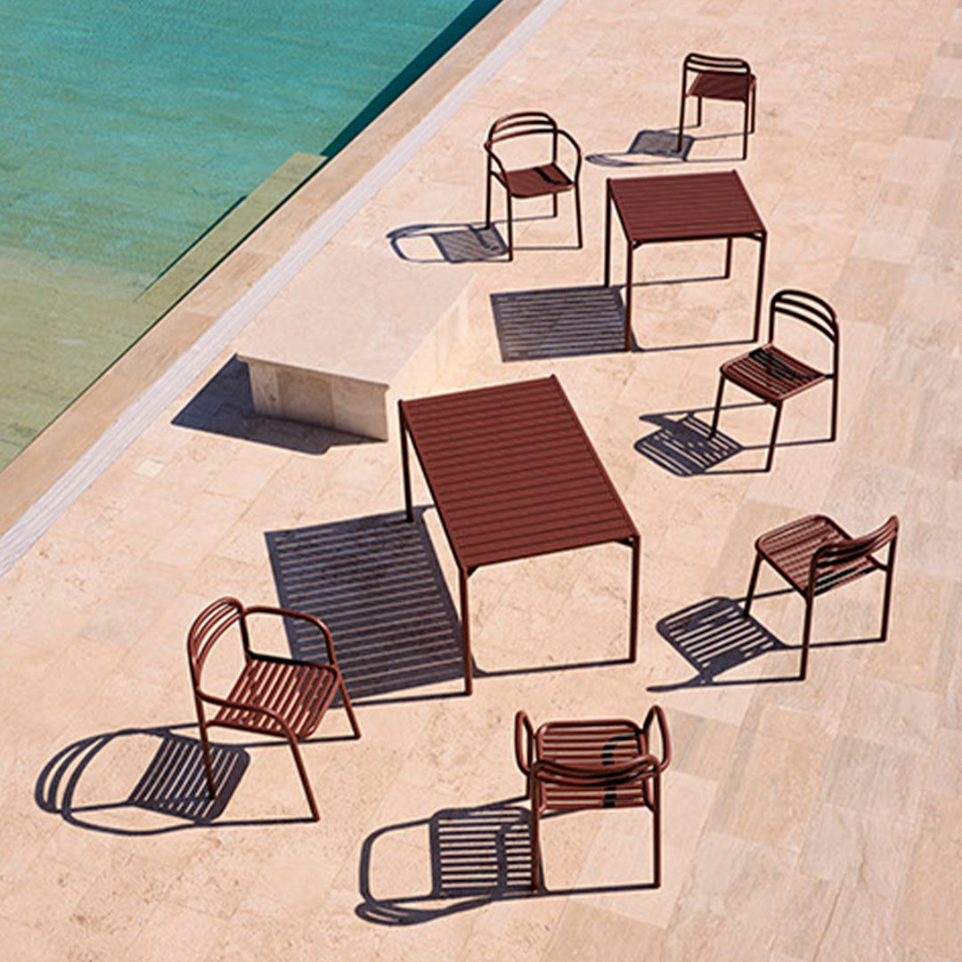 Rust-colored outdoor furniture with striped patterns, arranged around a clear blue pool on a sunlit patio.