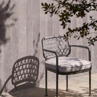 Gray outdoor chair with intricate woven pattern and soft beige cushion, casting a shadow on a textured surface.