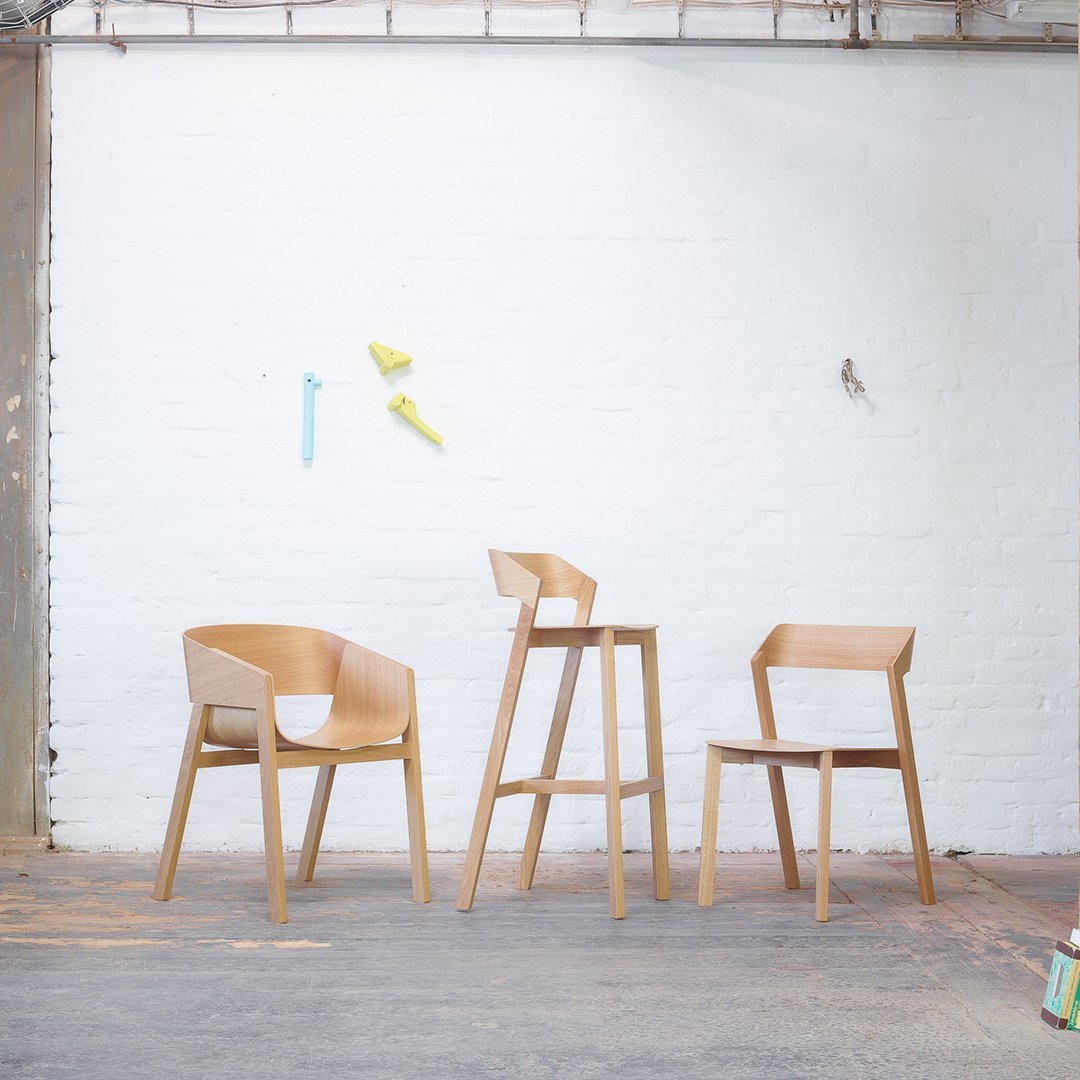 Light oak wood dining chairs and bar stool with minimalist design against a white wall and colorful accents.