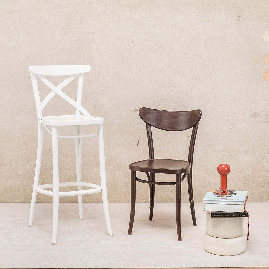 Two chairs: a white cross-back barstool and a dark brown traditional chair, styled against a neutral background.