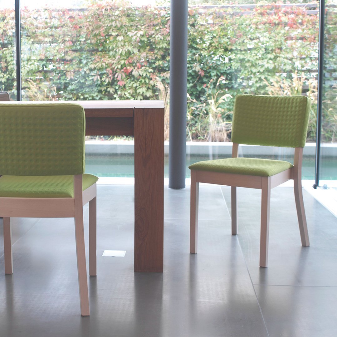 Set of two modern dining chairs with bright green textured fabric, paired with a natural wood table in a contemporary setting.