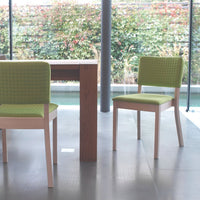 Set of two modern dining chairs with bright green textured fabric, paired with a natural wood table in a contemporary setting.