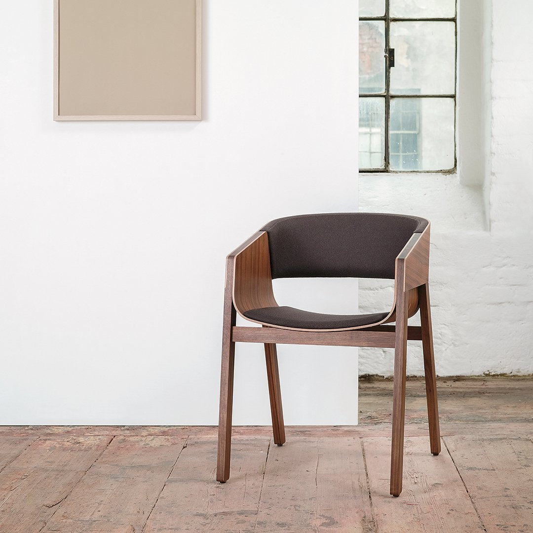 "Modern wooden chair with a dark brown fabric seat and minimalist design against a light wall."