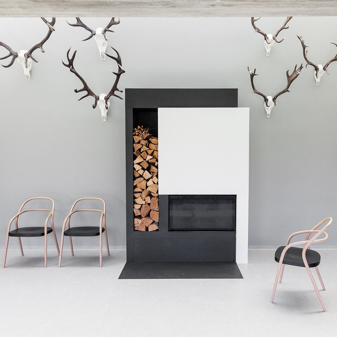 Modern fireplace in black and white, featuring stacked wood and minimalistic design. Elegant chairs with soft pink accents.
