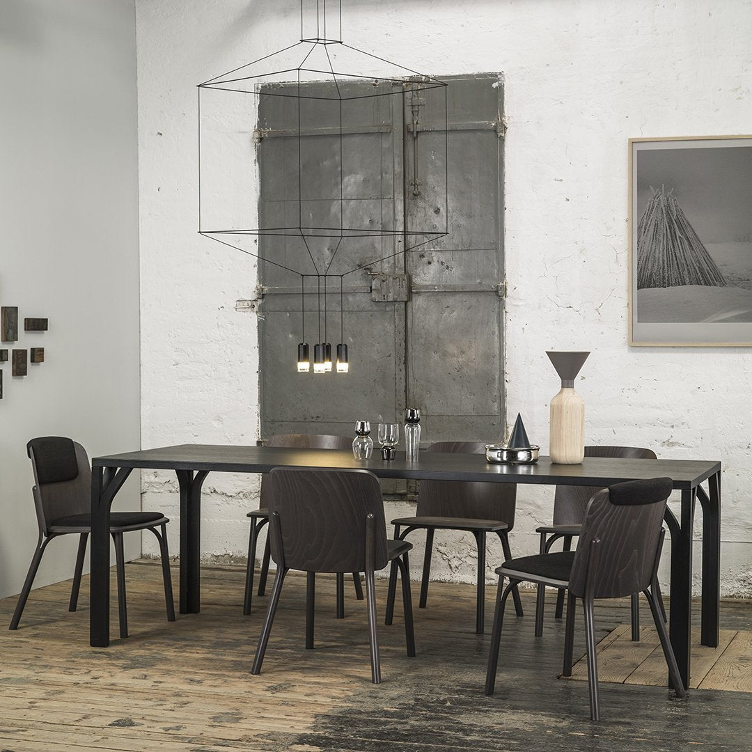 Modern black dining table with dark chairs, set against a rustic wood floor and minimalist gray walls for a sleek look.