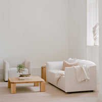 Neutral-toned sofa and armchair with light beige accents on a light wooden coffee table in a minimalistic setting.