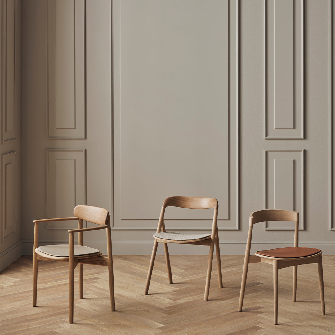 Wooden chairs in natural tones with minimalist design against a light gray paneled wall and warm wood flooring.