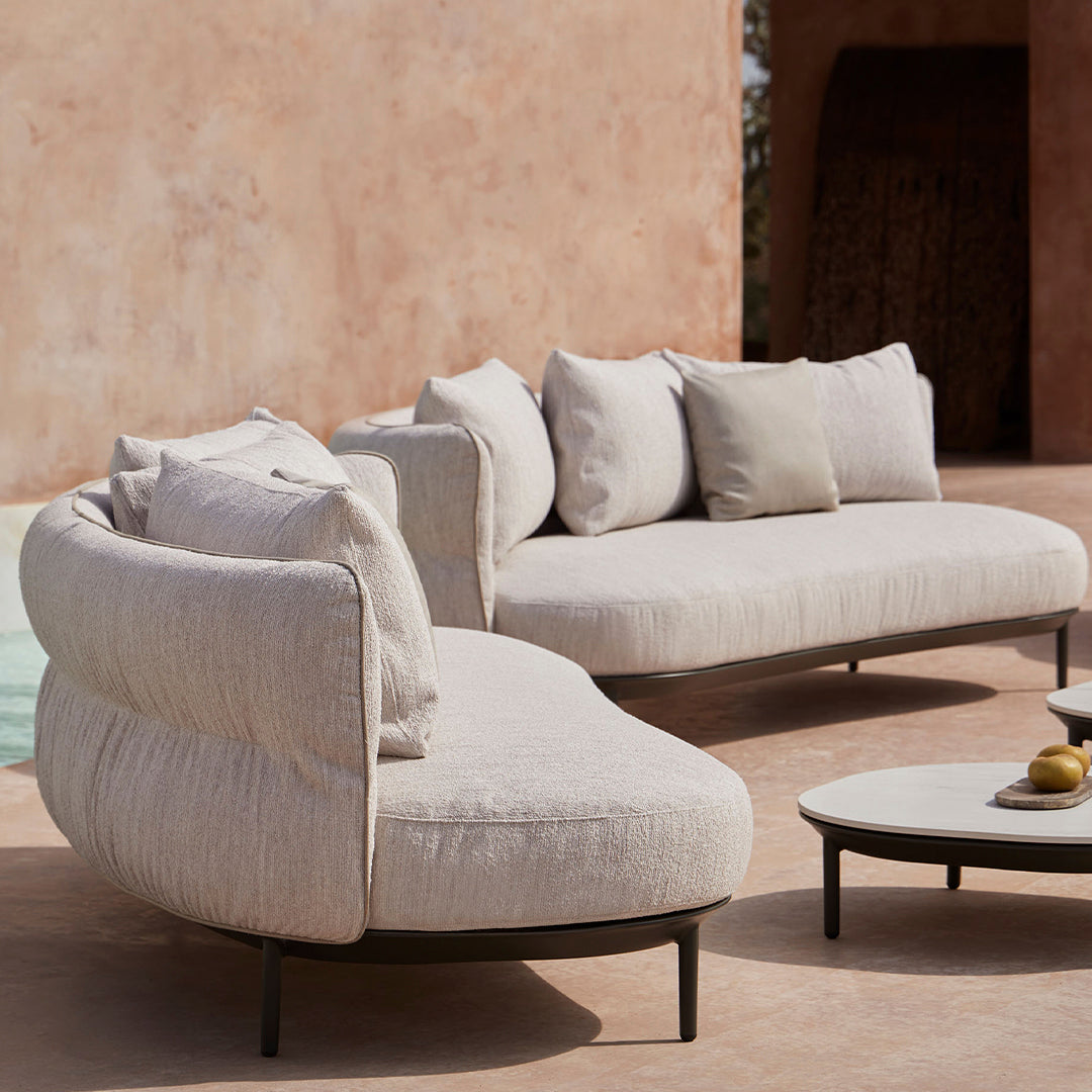 Light beige curved sofa with textured fabric and neutral throw pillows, paired with a minimalist round coffee table.