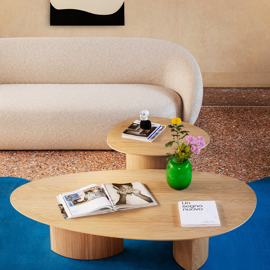 Light beige sofa on blue carpet with wooden tables and a bright green vase, featuring floral patterns and natural textures.