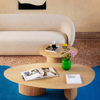 Light beige sofa on blue carpet with wooden tables and a bright green vase, featuring floral patterns and natural textures.