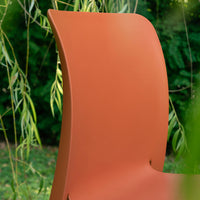 Curved orange chair against a lush green background, showcasing a modern minimalistic design.
