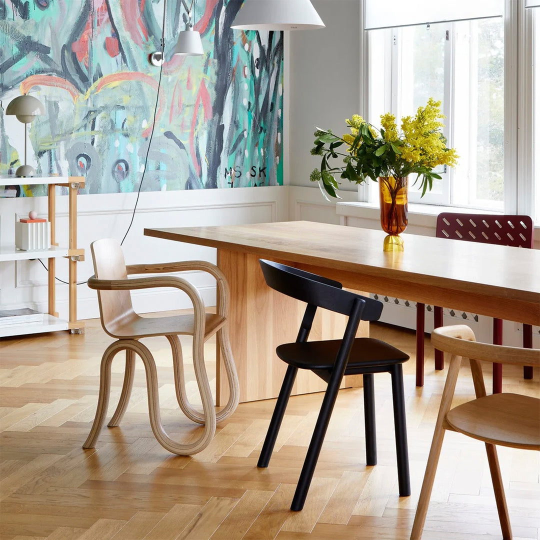 Modern dining area featuring colorful abstract wall art, light wood tones, and black and red chairs.