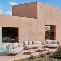 Beige outdoor sectional sofa with subtle texture, paired with neutral-toned tables against a soft clay-colored backdrop.