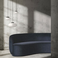 "Curved navy sofa with soft texture, set against a minimalist gray backdrop and accented by three white pendant lights."