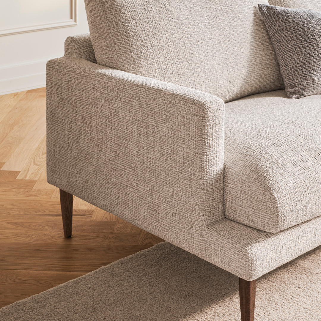 Light beige textured sofa with a soft, woven fabric and subtle pattern, complemented by wooden legs and accents.