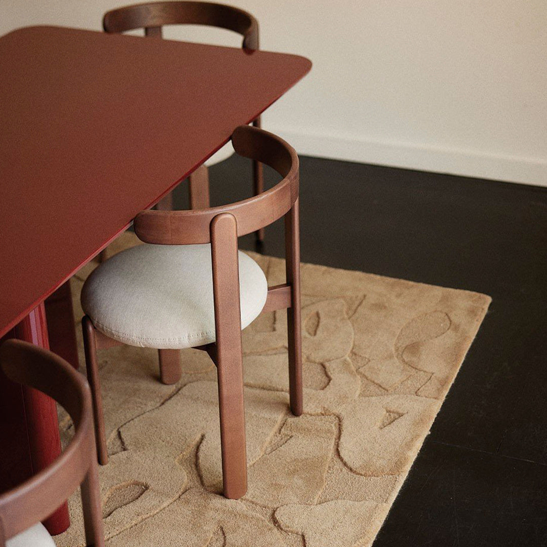 Maroon dining table with sandy beige chairs and patterned natural fiber rug in a stylish indoor setting.