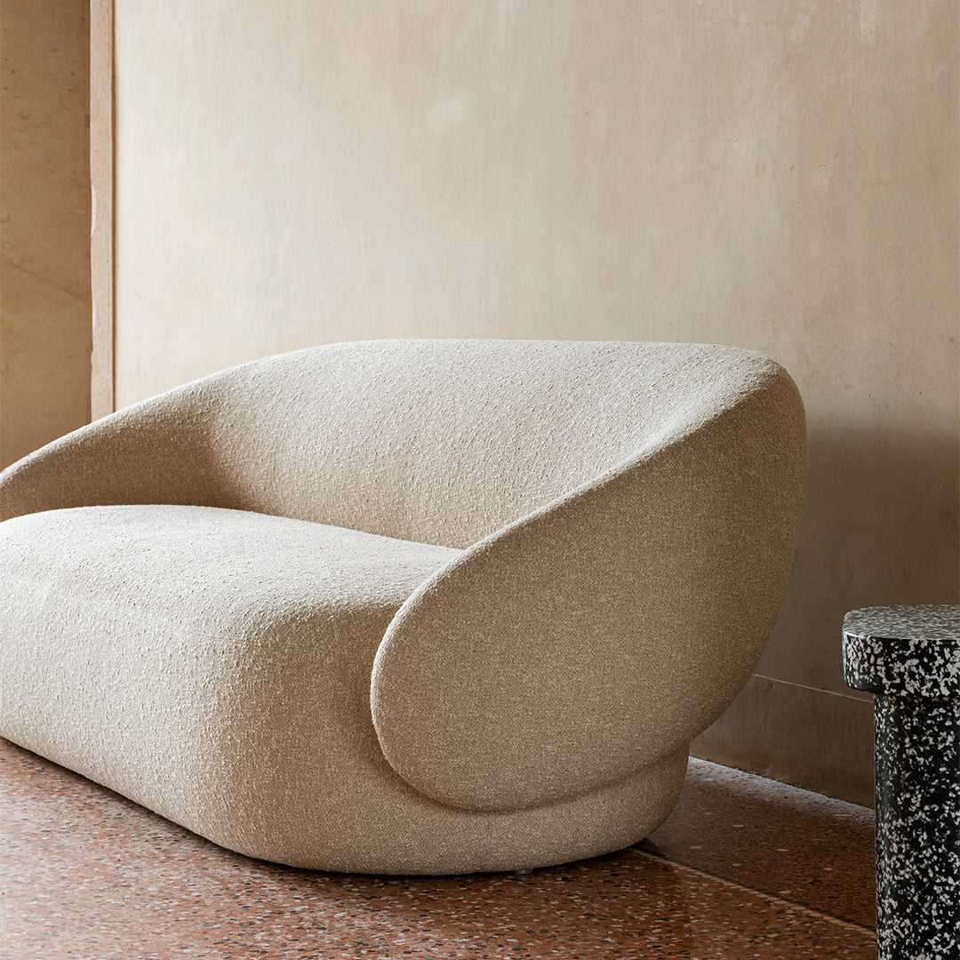 Beige textured fabric sofa with soft curves and seamless design against a neutral wall and mosaic flooring.