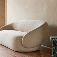 Beige textured fabric sofa with soft curves and seamless design against a neutral wall and mosaic flooring.