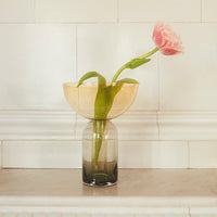 "Elegant two-tone glass vase in amber and gradient gray with green leaves and pink flower, set on a marble surface."
