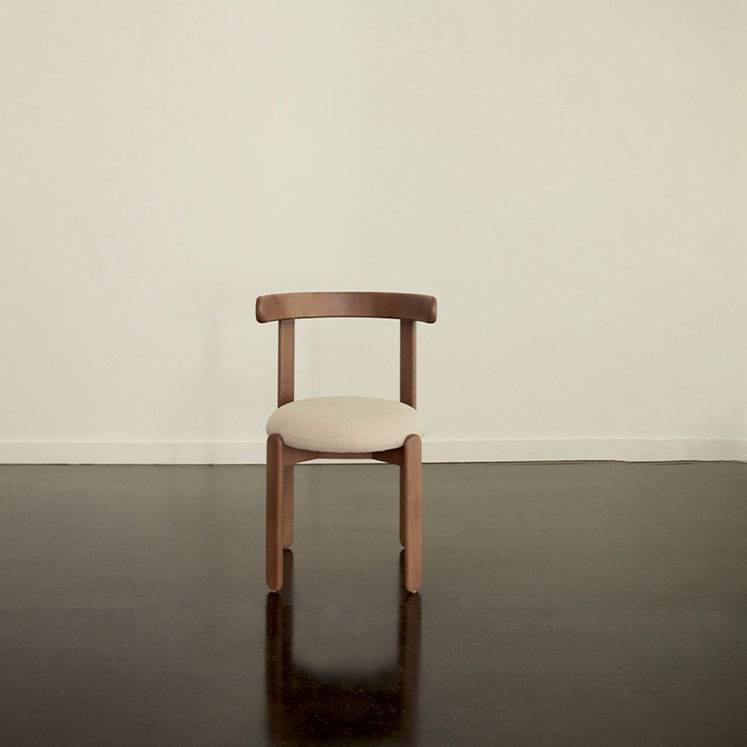 Natural wood chair with a minimalist design and beige upholstered seat against a smooth, light-wall background.
