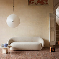 Soft beige sofa with textured fabric, round white pendant light, and light wood table against warm-toned walls and flooring.