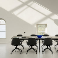 Minimalist workspace featuring black chairs, a wooden table, and a vibrant blue bowl against a neutral backdrop.