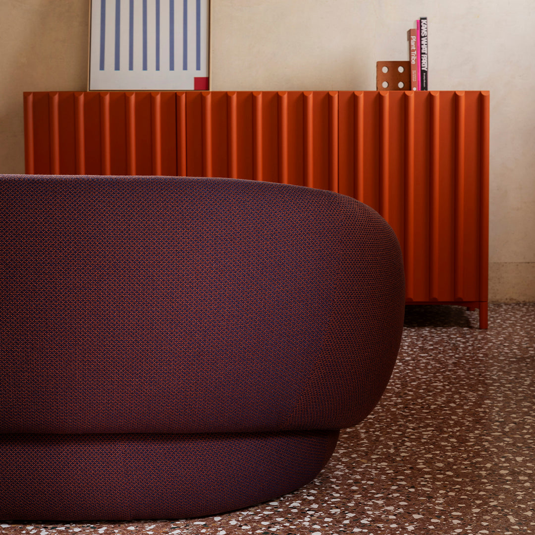 Textured burgundy upholstery with a sleek orange ribbed cabinet against a warm neutral background.