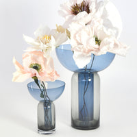"Blue and grey glass vases with delicate pastel flowers in soft pink and white, featuring elegant shapes and smooth finishes."