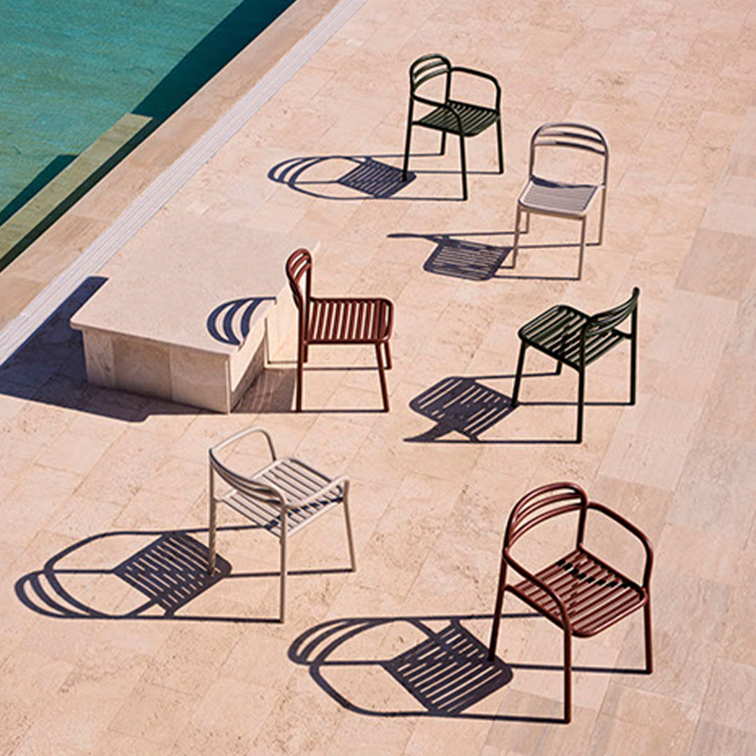 Colorful outdoor chairs in green, red, white, and beige with striped patterns, casting playful shadows on stone.