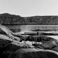 Sleek silver metal chair and table on rocky shore, contrasting against the dark water and light gray rocks.