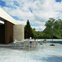 Elegant outdoor dining set with neutral beige chairs and table, surrounded by a serene blue pool and lush greenery.