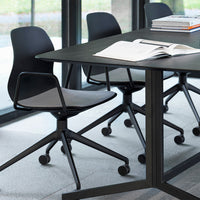 Black and gray ergonomic chairs around a sleek black table, set against a light stone floor and large glass windows.