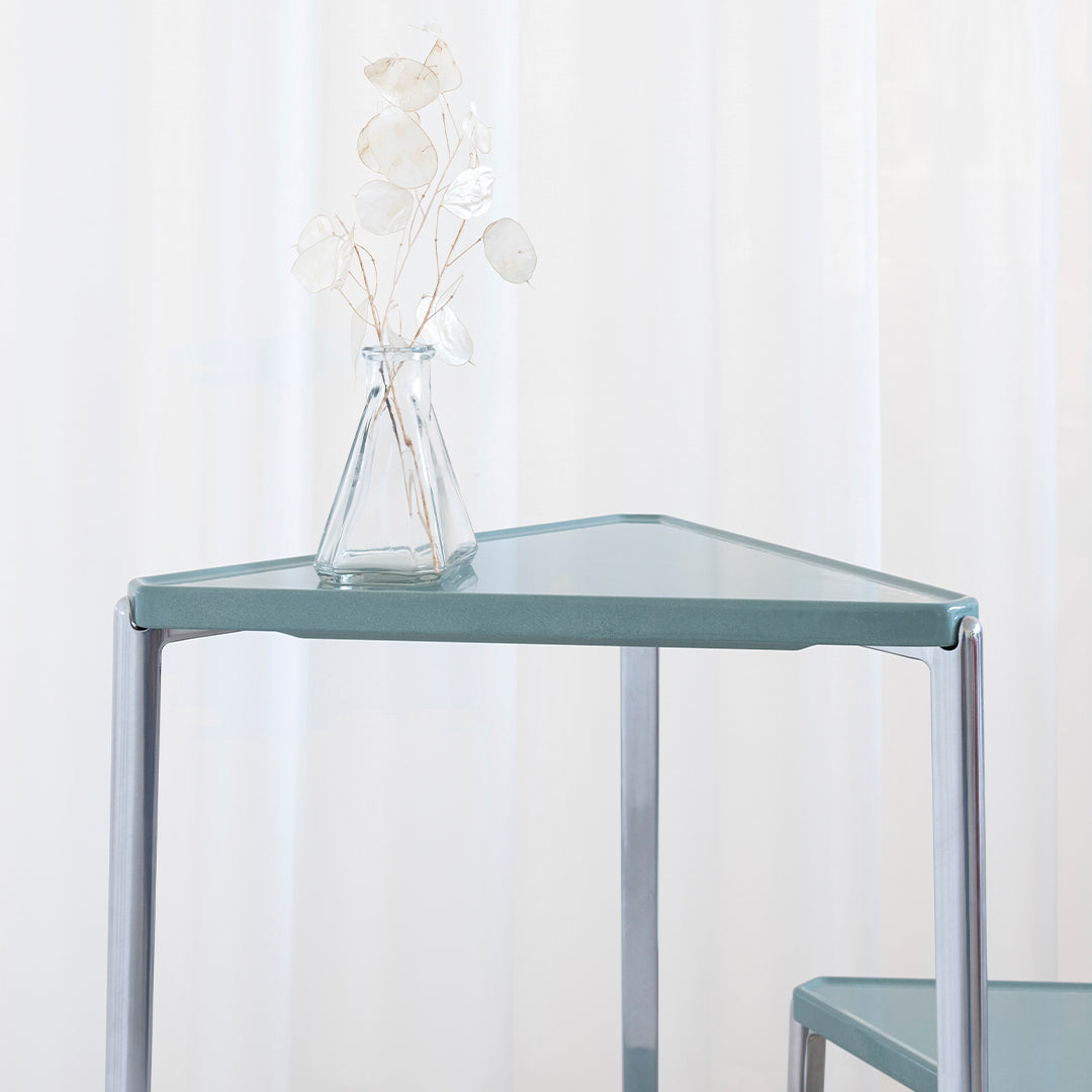 Triangular table with a soft green surface and chrome legs, showcasing a modern minimalist design.