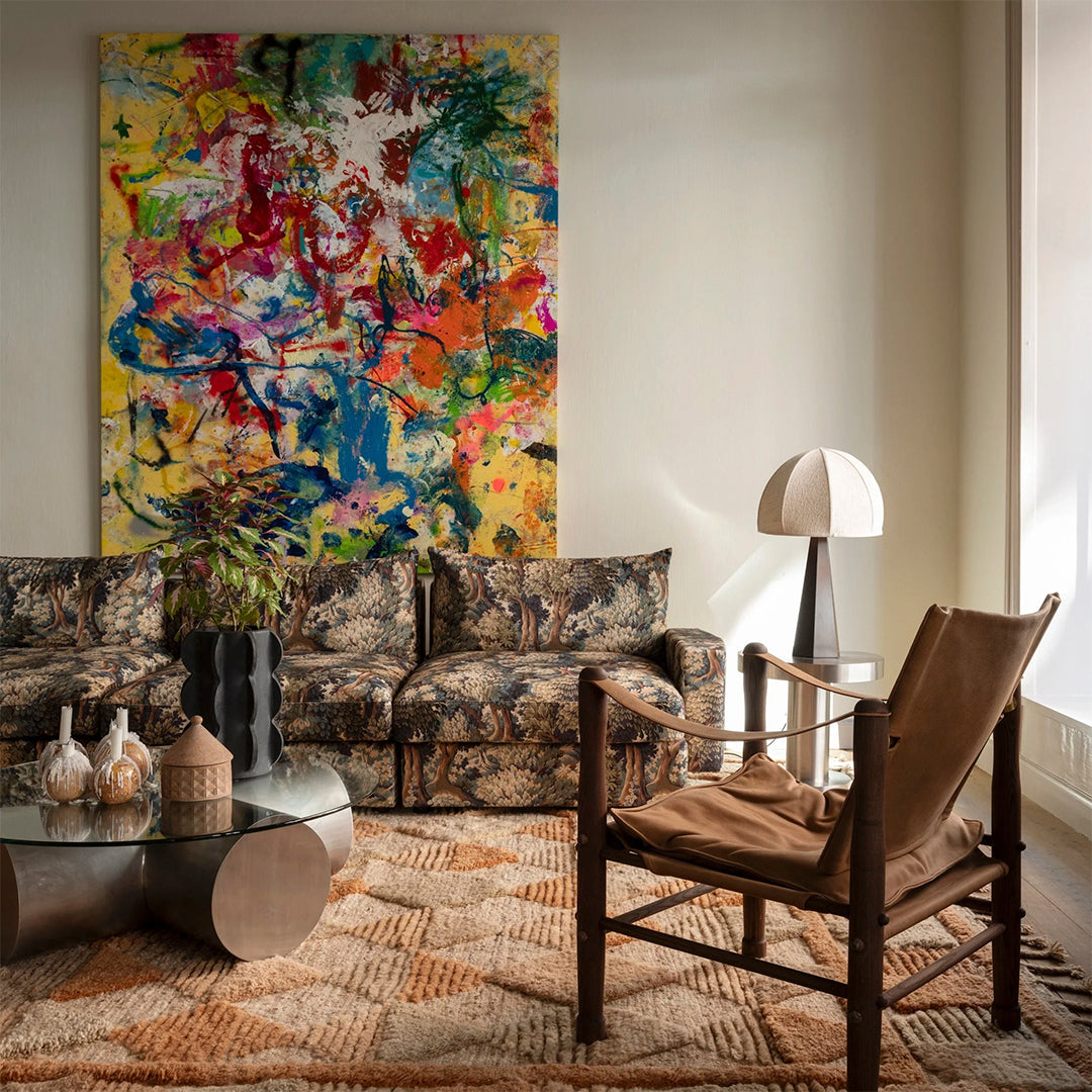 Colorful abstract art with vibrant yellow, blue, red, and green patterns above a vintage sofa in earthy tones.