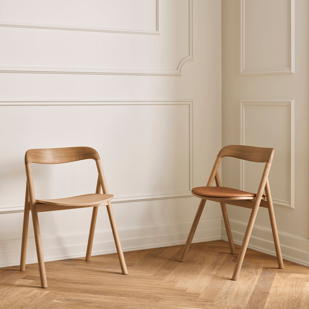 Natural wood finish folding chairs with a smooth, minimalist design, set against a neutral wall and light wood floor.