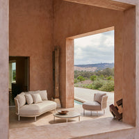 Stylish beige sofa and chair set with soft cushions, set against a warm terracotta wall and scenic outdoor view.