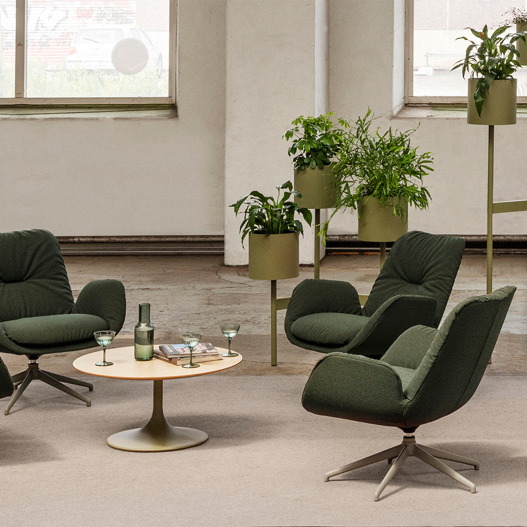 Green upholstered chairs, light wood table, and soft beige rug with potted plants in modern, neutral space.