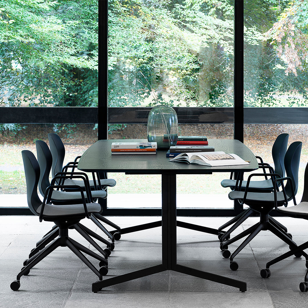 Modern black table with textured surface, surrounded by blue-gray chairs, bright natural light from large windows.