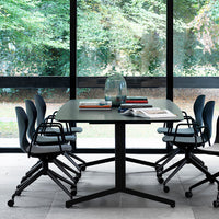 Modern black table with textured surface, surrounded by blue-gray chairs, bright natural light from large windows.