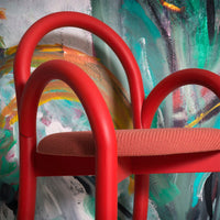 Red chair with curved arms and a textured coral seat against a vibrant abstract painted background.