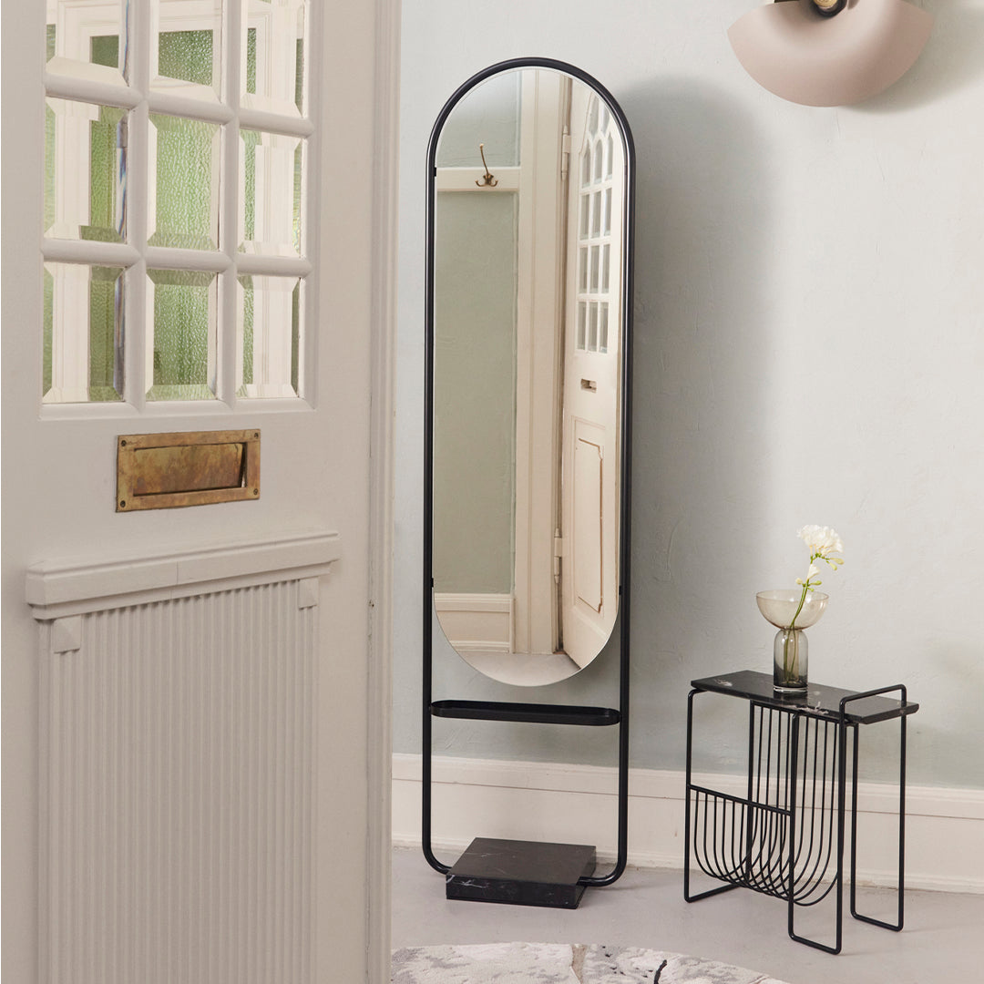 Full-length mirror with a sleek black frame and marble base, set against a soft pastel wall. Modern, minimalistic design.