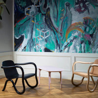 "Modern chairs in black, natural wood, and a pink table against an abstract teal and multicolor wall."