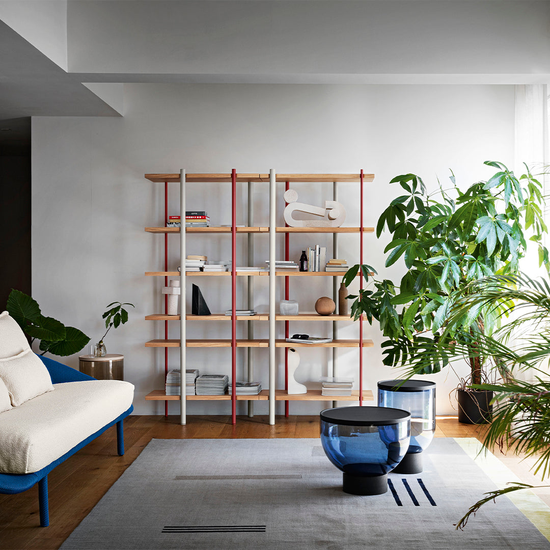 Modern bookshelf with light wood shelves, red and white accents, complemented by blue and gray furnishings.